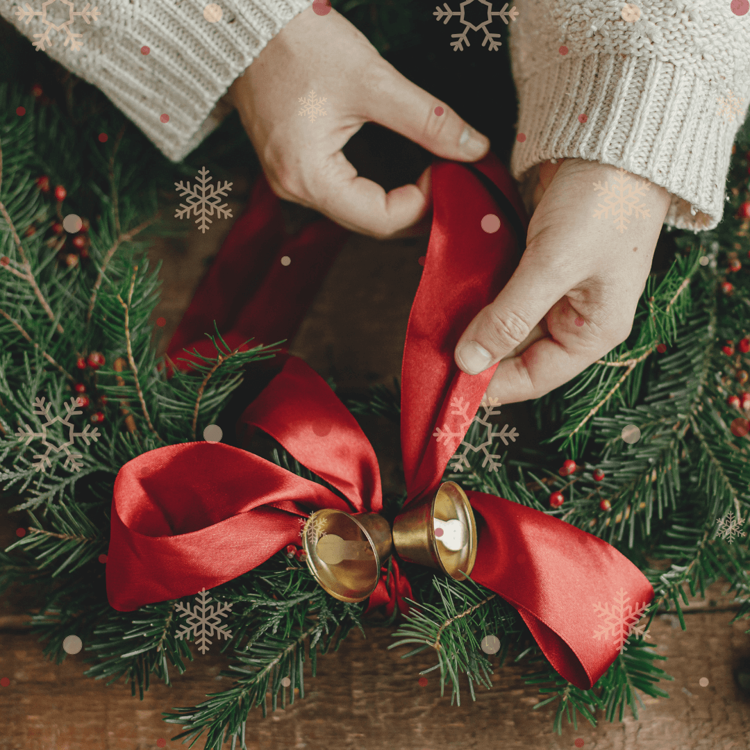 Hands shown tying a red ribbon on a Classic Runyans Wreath.